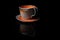 A clay ceramic mug with a saucer is placed on a black base with a reflection...The lower part of the mug has a coarse layer of