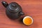 Clay glazed bowl with brewed tea and clay teapot on red wooden table, focused on bowl