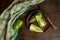 Clay plate with whole and halves of green bell pepper and green kitchen towel on wooden background