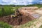 Clay quarry. The yellow excavator digs red clay with a large bucket and puts it into the truck