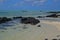 The clean clear transparent sea water off Ile aux Cerfs Mauritius with emerged black rocks and visible sandy beach