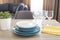 Clean dishes on the table. Stacked clean blue and white plates, glasses and yellow napkins on wooden table in the kitchen.