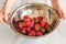 Clean red ripe strawberries in a stainless steel colander are rinsed under water in a woman hand.