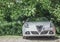 Clean shining silver Alfa Romeo Giulietta parked under a green tree. Beautiful bright sunny day. Front view of the car grill on