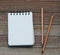 Clean unlined notepad laying on a wooden background with pencils