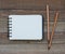 Clean unlined notepad laying on a wooden background with pencils