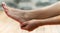 Clean woman foot and her right hand touching her heel, background of wood and stone