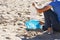 Cleaning beach from plastic trash. Hand picking up plastic bottle from the sand and putting into plastic bag for recycle