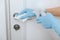 Cleaning black door handle with an antiseptic wet wipe, blue gloves and sanitizer. Sanitize surfaces prevention in