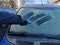 Cleaning car windows in winter. Man scrapes hoarfrost with a plastic scraper from thewindshield of a blue car. Close-up.