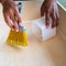 Cleaning and home concept - close up of male brooming wooden floor with small whisk broom and recycled milk boxes as dustpan