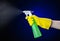 Cleaning the house and cleaner theme: man\'s hand in a yellow glove holding a green spray bottle for cleaning on a dark blue