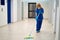 A cleaning lady with the mask on her face mops the floor in an office building