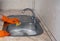 A cleaning lady in orange rubber household gloves washes a sink with a yellow sponge.