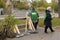 Cleaning parks: female municipal sweepers standing beside row of rakes leaned against bench