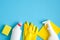 Cleaning supplies on blue background. Top view cleaner spray bottle, rag, yellow sponge, detergent, rubber gloves. House cleaning
