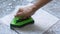 Cleaning the tiled floor with a green color plastic floor scrubber.