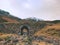 Clear curved stream river below old stony bridge. Mountain sheep path