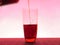 In a clear glass filled with a dark fizzy drink. Photo on a pink background