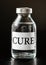 Clear glass vaccine bottle with label CURE black background