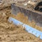 Clear Square Close up of a metal grader blade against the ground with brown soil