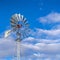 Clear Square Shiny steel windpump against a vibrant blue sky with cottony clouds