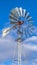 Clear Vertical Shiny steel windpump against a vibrant blue sky with cottony clouds