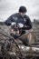 In a clearing, a man cuts a tree trunk with a chainsaw to harvest firewood. A strong man with a chainsaw is sawing up