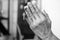 Clenched hands of the elderly woman with Jesus Christ holy cross crucifix in prayer pose gesture. On Black and white background.