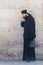 The clergyman stands and talks on his mobile phone in the old city of Jerusalem, Israel.