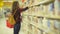 Clever Beautiful Girl with Glasses Holding Book in Her Hand in the Supermarket. Cute Woman Takes One Tome from a Shelf