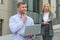 Clever businessman with laptop ahead of business lady who talking to him outdoor