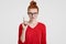 Clever freckled foxy student gets brilliant idea in mind, raises index finger in eureka gesture, wears transparent glasses, red sw