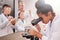 Clever mixed-race pupil in whitecoat and eyeglasses looking in microscope