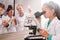 Clever serious schoolgirl in whitecoat looking in microscope at chemistry lesson