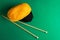 Clews of yellow black fine wool yarn wooden knitting needles on dark green background warm autumn color palette. Crafts hobby