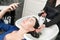 Client brunette woman looks at phone while hairdresser is busy washing her hair at beauty salon.