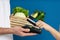 Client paying courier for fresh products with credit card on blue background, closeup. Food delivery service