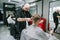 Client sits in a hairdresser`s chair and uses a smartphone when the barber creates a stylish haircut with a hair clipper in his