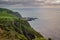 Cliff with vegetation and green field overlooking the hot sea springs of Ponta da Ferraria in lava fajÃ£ at sunset, SÃ£o Miguel