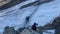 A climber in a blue jacket walks along the moraine, moving along a rope with a belay.