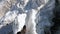 A climber in a bundle is walking along a narrow snow bridge past deep cracks on both sides. First-person view.