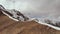 Climber climbs uphill with a backpack and trekking sticks on the ridge at the junction of stone and snow. Aerial view