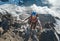 Climber in a safety helmet, harness with backpack ascending a rock wall with Bionnassay Glacier on background and looking at the