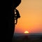 Climber silhouette rock climbing on cliff. Orange sky with sunset on horizon with wide valley on background. Copy space