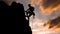 A climber is silhouetted against the evening sky as he clings to a steep rock face