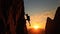 A climber is silhouetted against the evening sky as he clings to a steep rock face