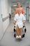 Clinic employee carries smiling woman in wheelchair along hospital corridor