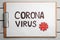 Clipboard with words CORONA VIRUS on white wooden background, top view