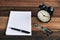 Clock, glasses, pen and blank notebook on a wooden table